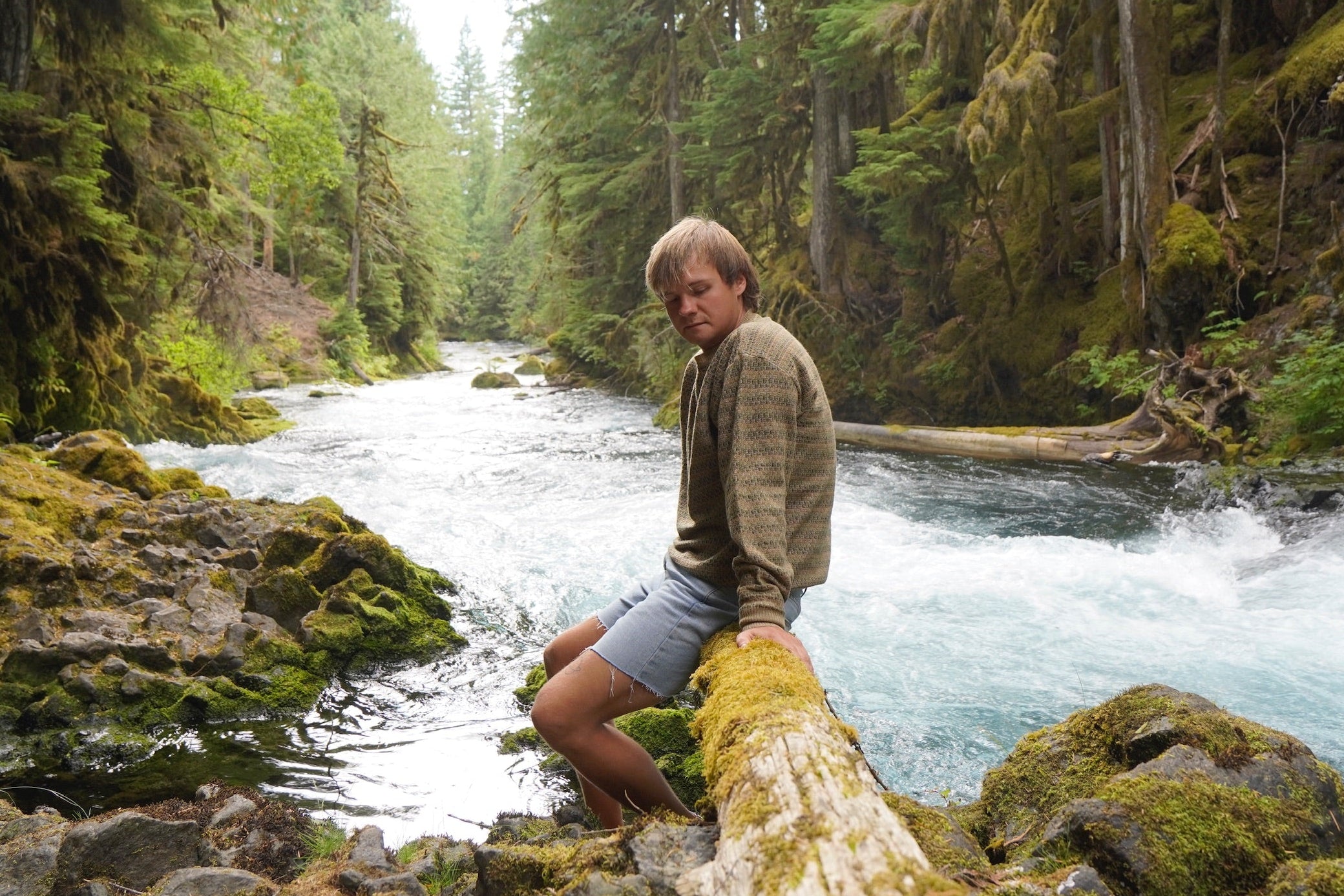 kyle sitting on a log by a river in a forest