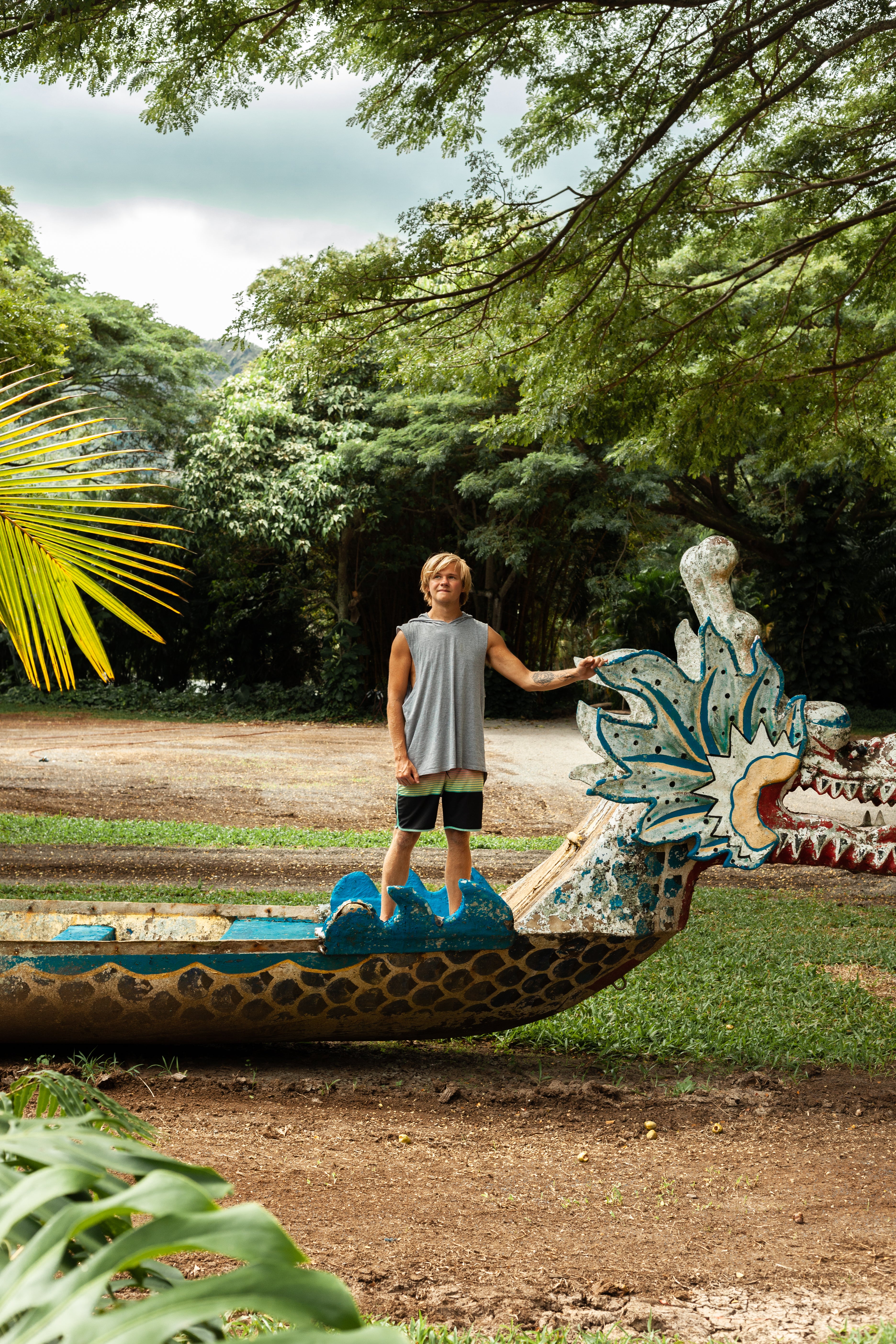 kylegoesoff standing next to a colorful dragon sculpture in a park-like setting with trees and plants.