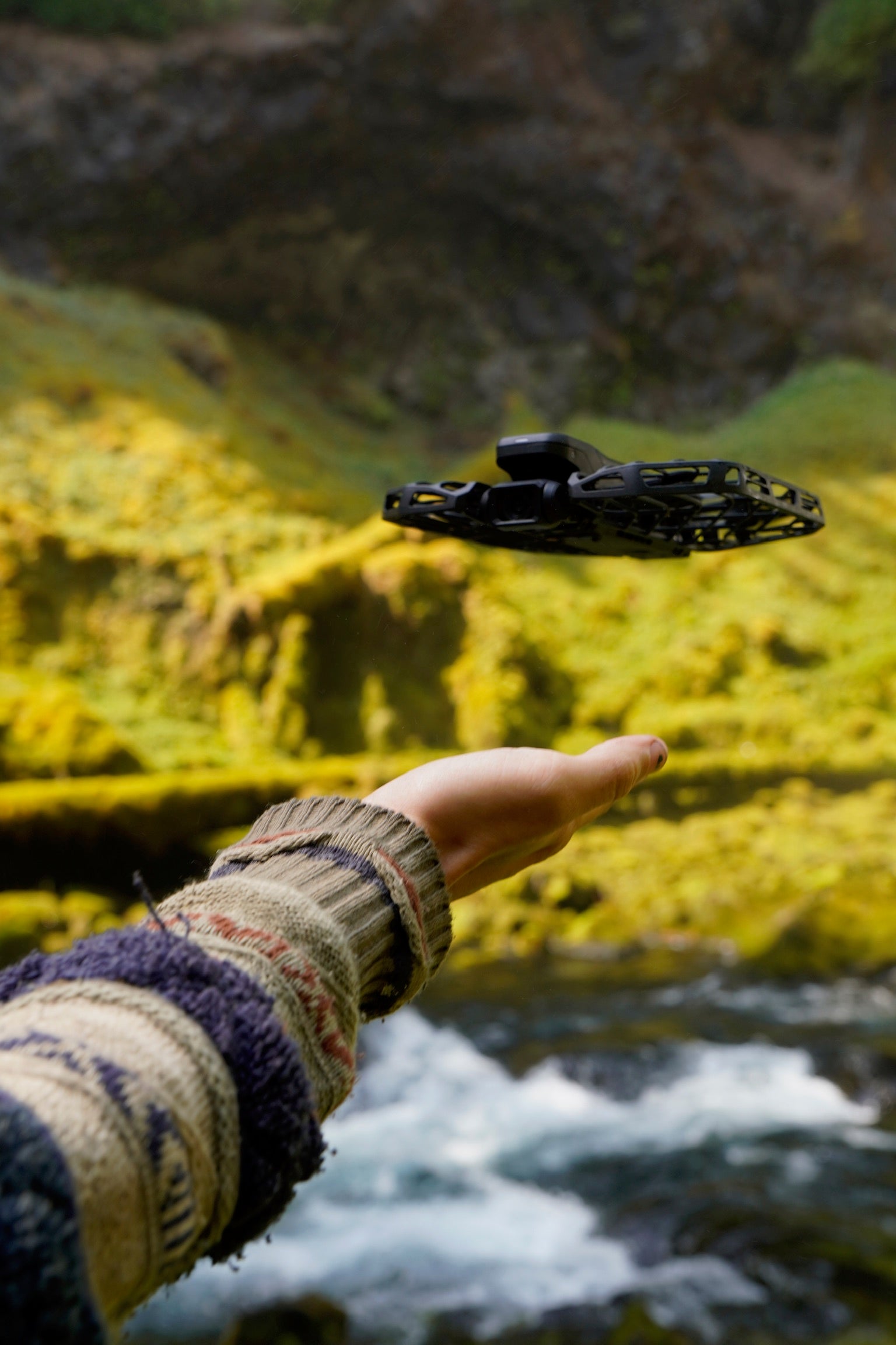 Person holding a black disc brake rotor against a natural background with water and rocks.